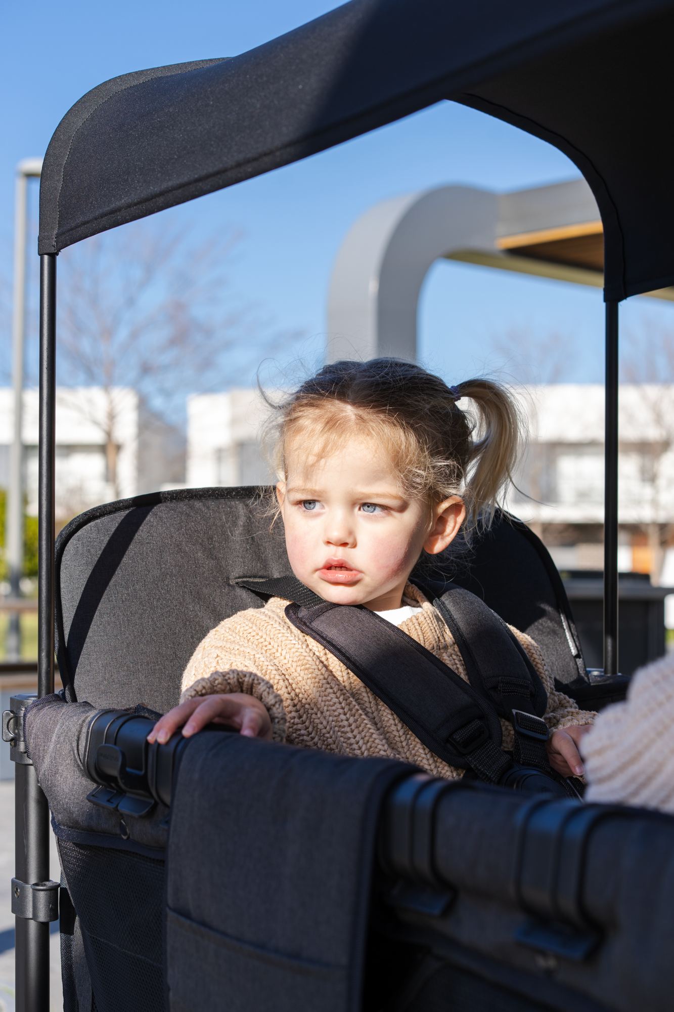 A toddler in a knitted jumper sits harnessed in a WonderFold