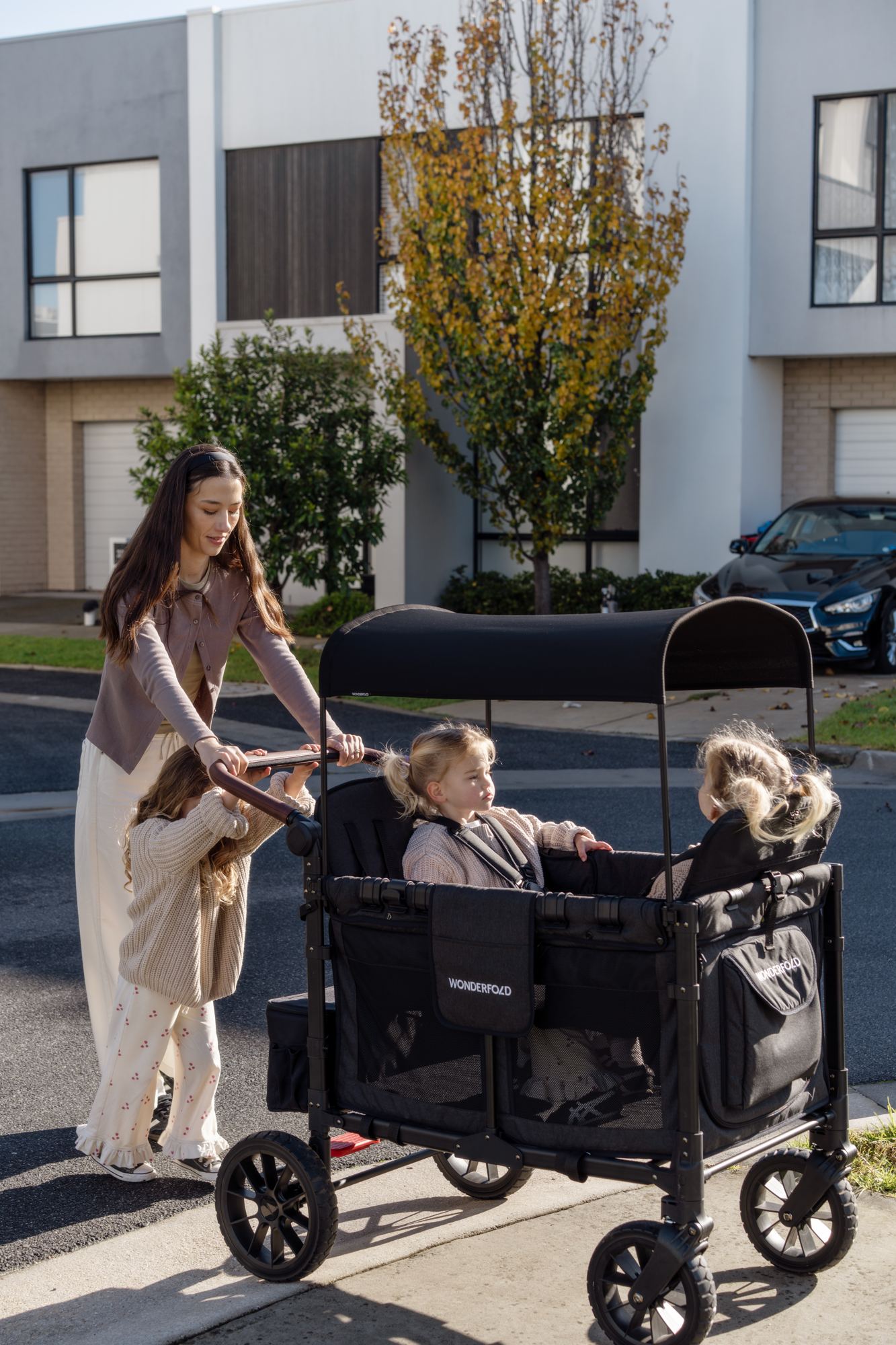 A mother pushes twin girls in a WonderFold along a suburban street