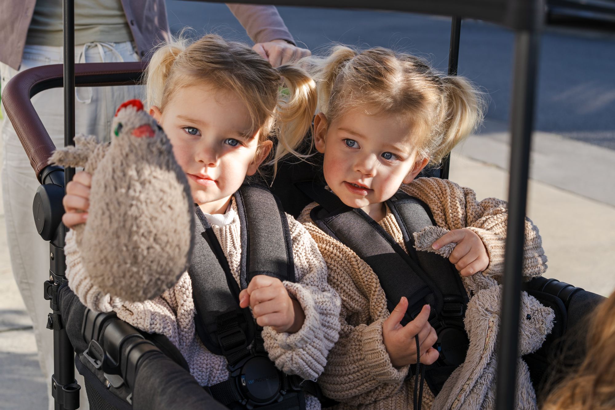 Twin girls sit side by side in a WonderFold, one holding a toy chicken