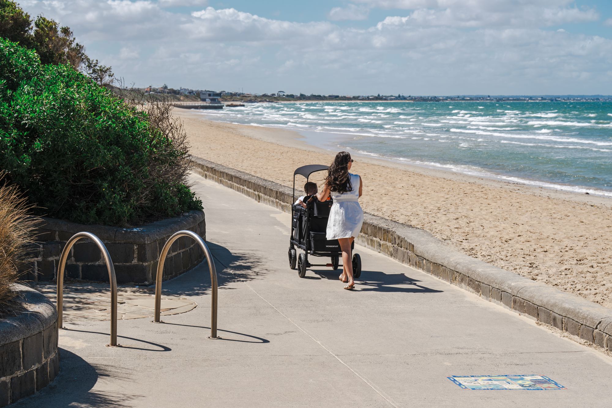 A mother pushes a WonderFold along a beachside path