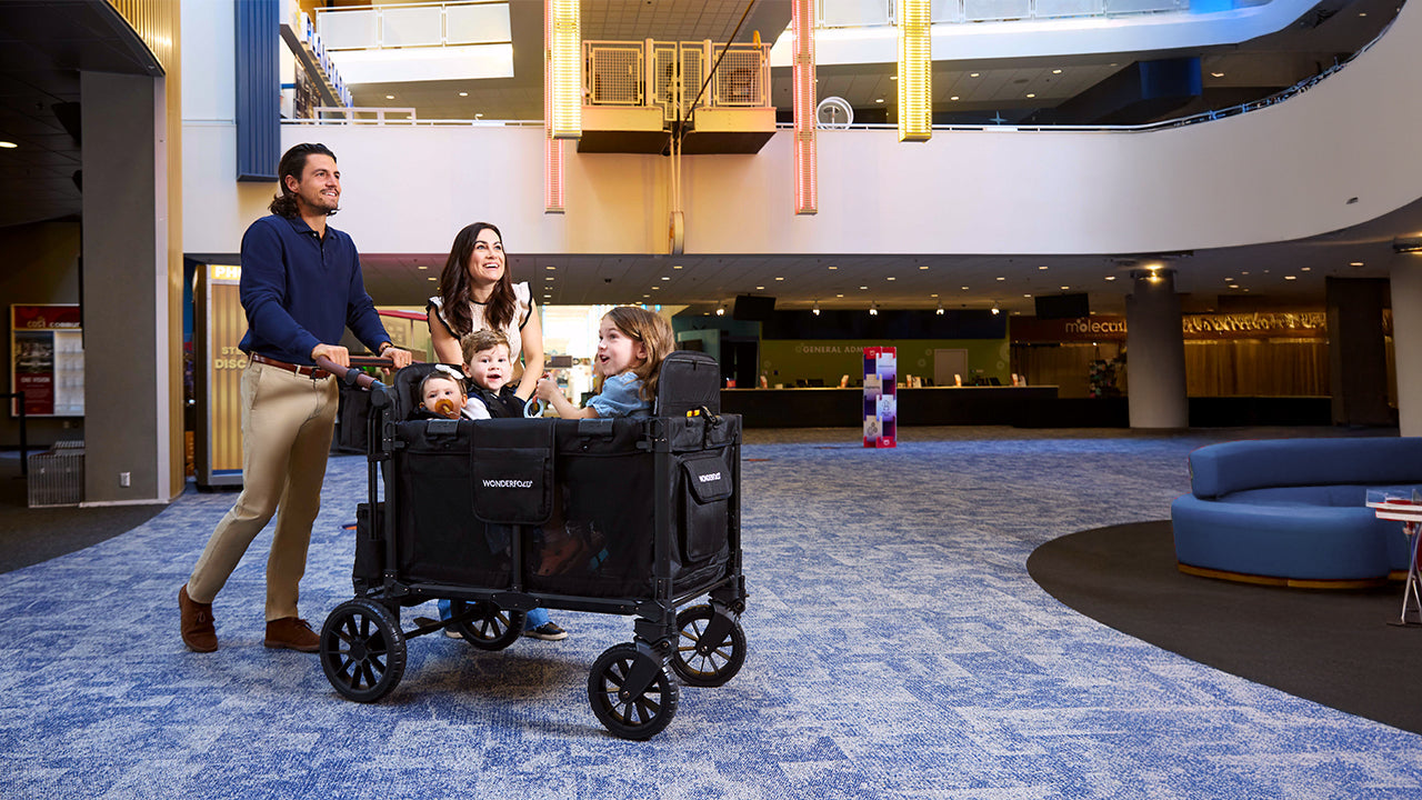 A family pushes three children in a WonderFold W4 through a museum foyer