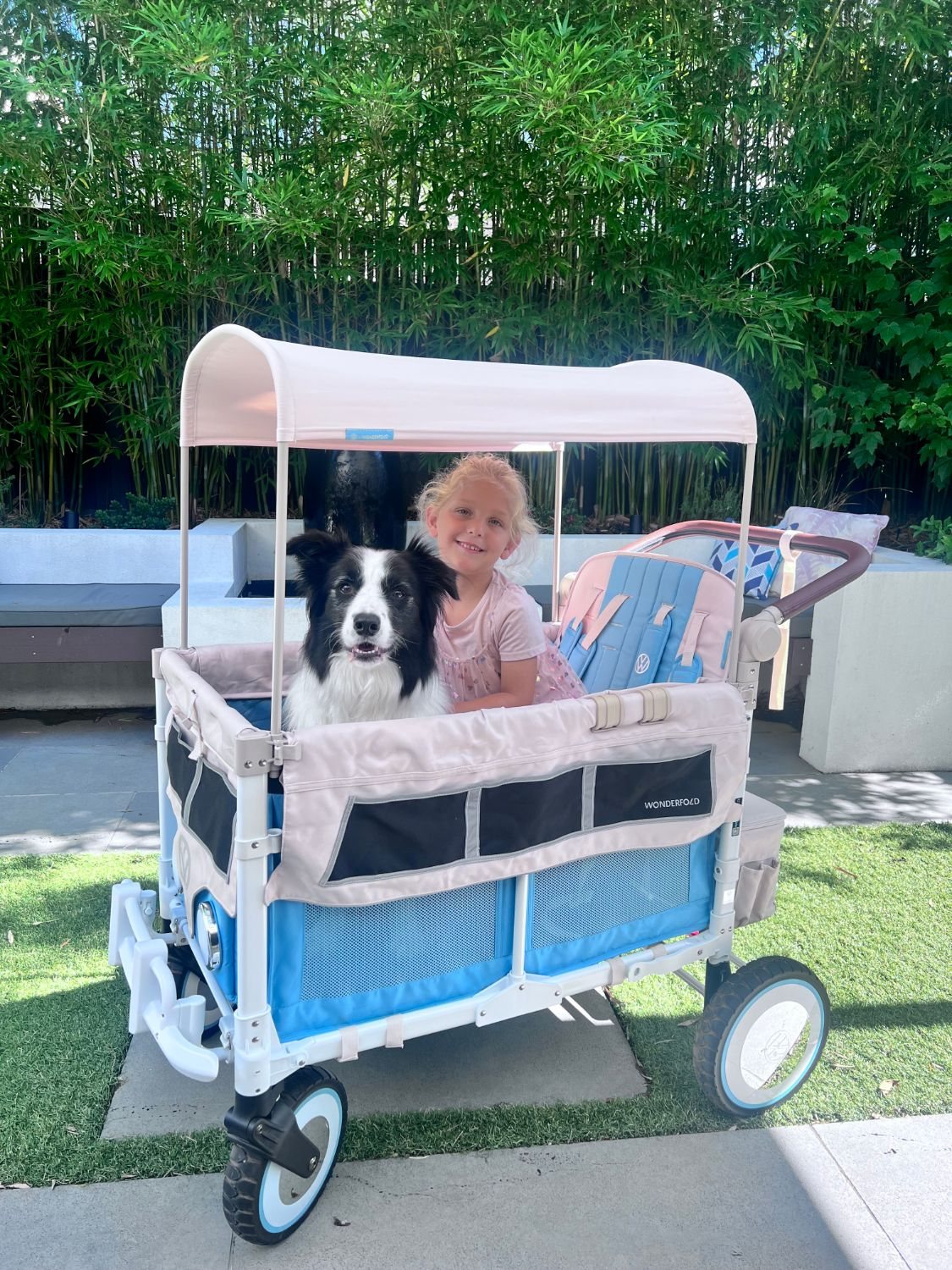 A smiling girl and a border collie sit in a WonderFold W4 Volkswagen special edition in Bondi Blue in a backyard